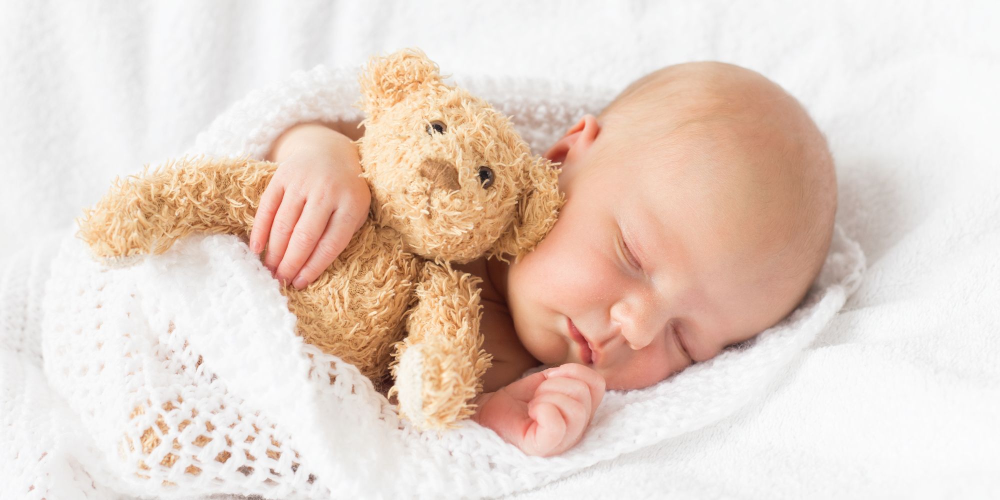 Bébé endormi, tenant un ours en peluche, illustrant l'importance d'un sommeil calme et profond.