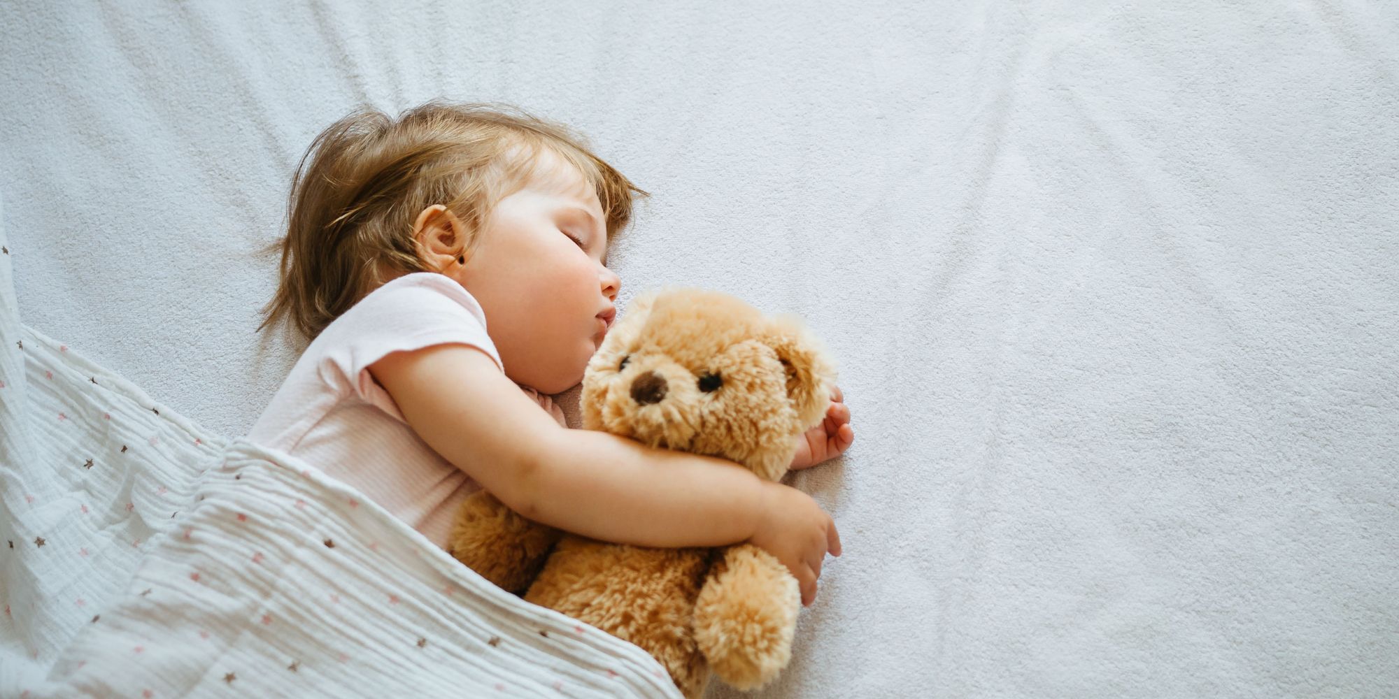 Bébé endormi paisiblement avec une peluche, symbole d'un sommeil réparateur.